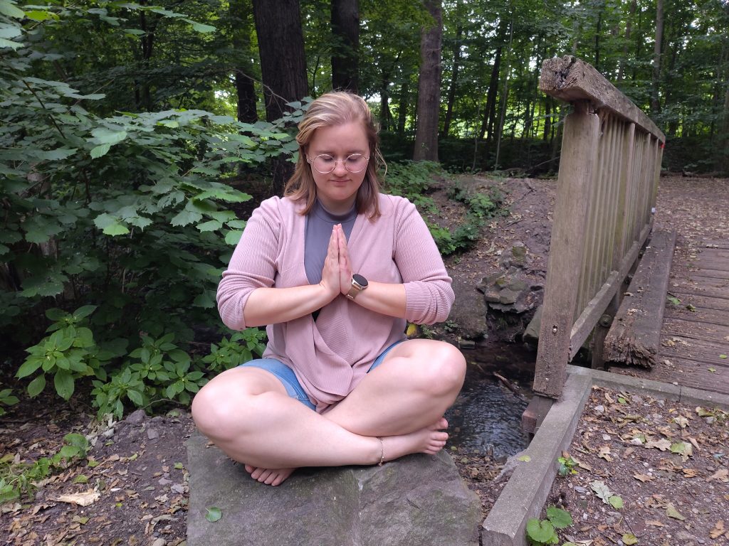 Frau sitzt im Wald auf einem Stein und meditiert