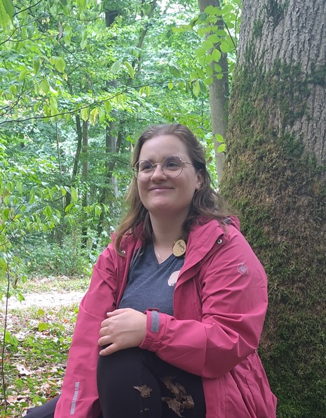 Frau sitzt an einem Baum im Wald und lächelt